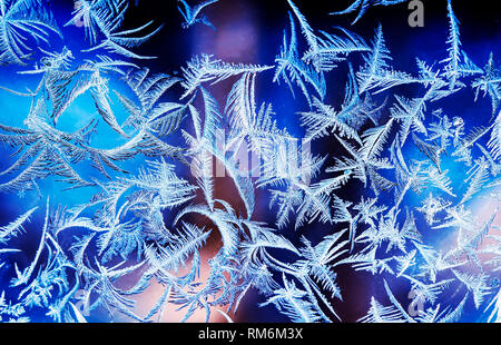 beautiful frosty pattern with various ornate patterns on the transparent glass on the winter window in delicate lilac and blue tones Stock Photo