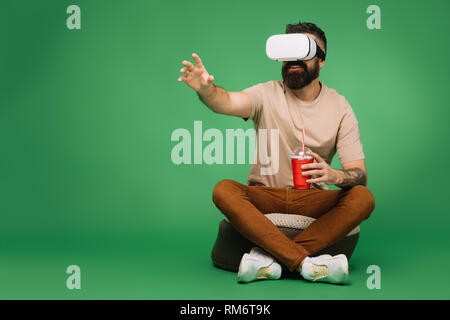 bearded man with soda using Virtual reality headset isolated on green Stock Photo