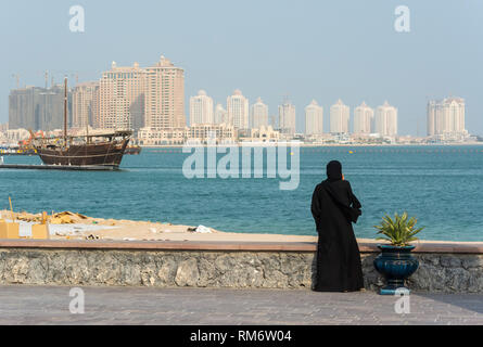 Street scene in Doha, Qatar with lady wearing traditional Qatari black dress and head cover with the Pearl district skyscrapers in the background. Stock Photo