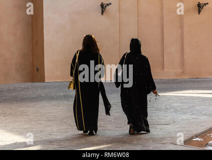 Two unidentifiable Arabic women wearing traditional Islamic black dress  walking away, from the back. One with covered and one with uncovered head. Stock Photo