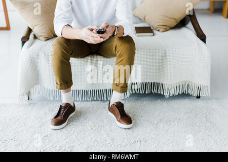 cropped view of senior man sitting on sofa and holding remote control Stock Photo