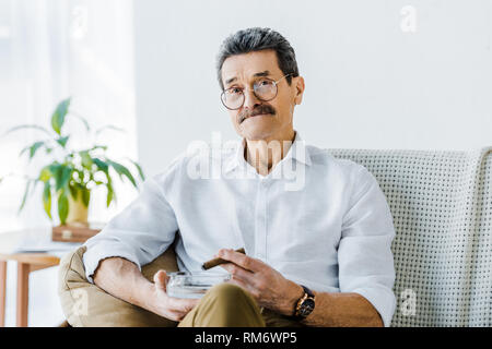 senior man with mustache holding sigar and ashtray in hands Stock Photo