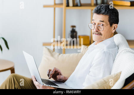 surprised senior man using laptop while sitting on sofa Stock Photo