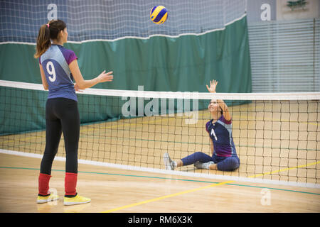 Sports for disabled people. Two young women playing volleyball. Woman ready to hit the ball. The ball in the air Stock Photo