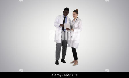 Intellectual healthcare professional afro american doctor with collegue using digital tablet on gradient background. Stock Photo