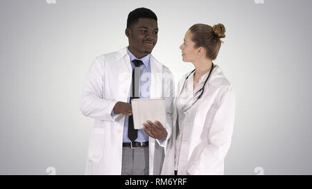 Intellectual healthcare professional afro american doctor with collegue using digital tablet on gradient background. Stock Photo