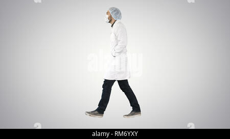 Walking doctor puting medical mask on on gradient background. Stock Photo