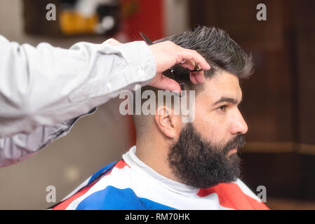 Handsome bearded man, having hair cut by scissors at barber shop . Stock Photo