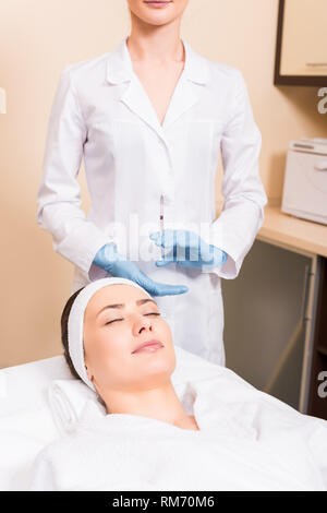 woman lying on massage table while beautician preparing injection in syringe at beauty salon Stock Photo