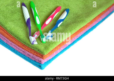 Four clean soft double bath towels set of different colors stacked and four toothbrushes isolated on white background. Side view from corner close-up Stock Photo