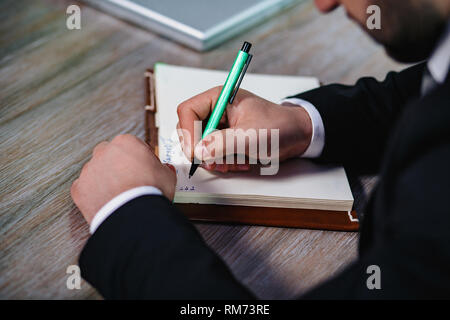 Man's hand in suit writing on notebook Stock Photo