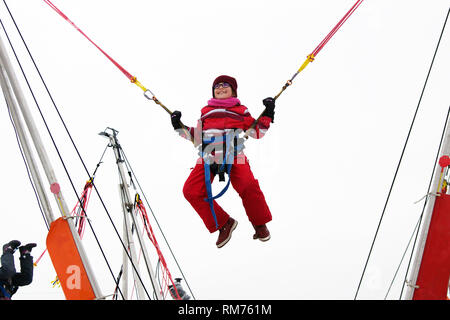 Little girl bungee jumping on trampoline during winter festival Stock Photo