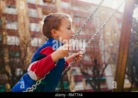 Happy child swinging in a city park with big smile. Stock Photo