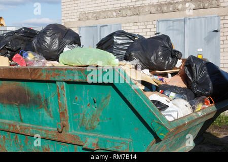 A large, metal, green garbage container and municipal waste, standing on a  dirt road near the fence and trees Stock Photo - Alamy