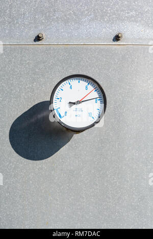 Close-up of a round gauge fitted on the wall of a large galvanized steel water tank, with blue figures and two red and black needles on a white dial. Stock Photo