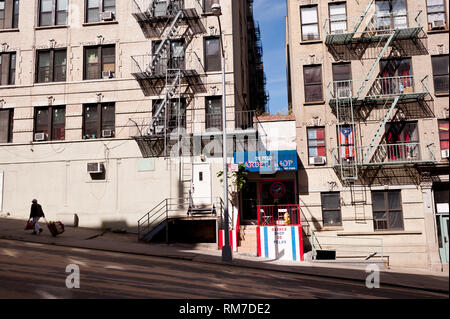Woman pulling luggage up steep hill Harlem area New York city ,with small barber shop squeezed between some residential buildings Stock Photo