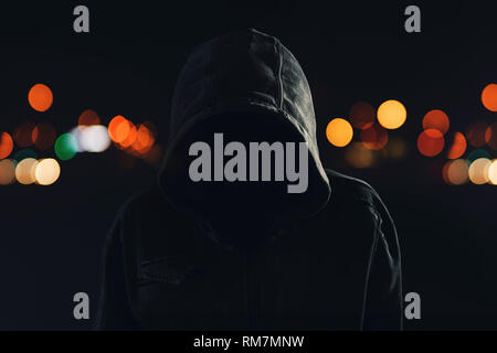 Hooligan with hoodie and obscured face walking the city streets at night, looking spooky and threatening Stock Photo