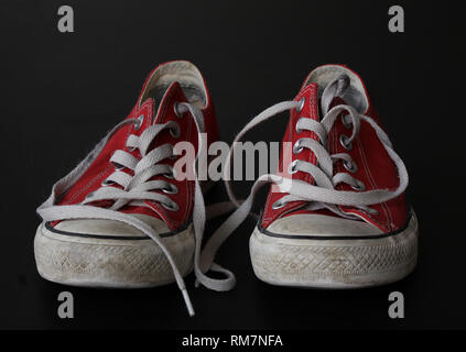 Close up of pair of sneakers - red and white vintage worn out shoes - youth hipster shoes on black background Stock Photo