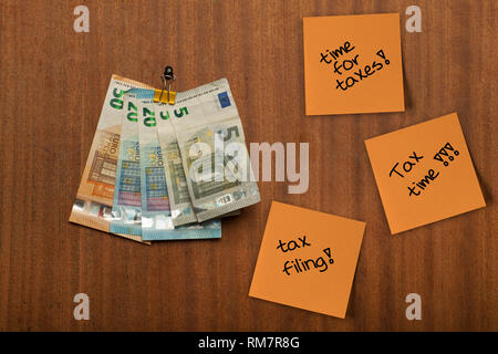 Several pieces of paper, post its hang on the wooden pin board and euro money,  notes , with the words taxes, time for taxes, tax time, filing written Stock Photo