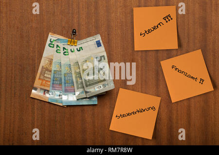 Several pieces of paper, post its hang on the wooden pin board and euro money,  notes , with the german words Steuern, Steuererklaerung, Finanzamt wri Stock Photo