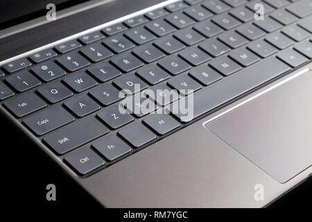 Part of opened laptop with keyboard, touchpad and empty mirror screen of black opened laptop isolated on black background side view closeup Stock Photo