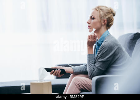 upset woman with tissue watching tv on couch at home alone Stock Photo