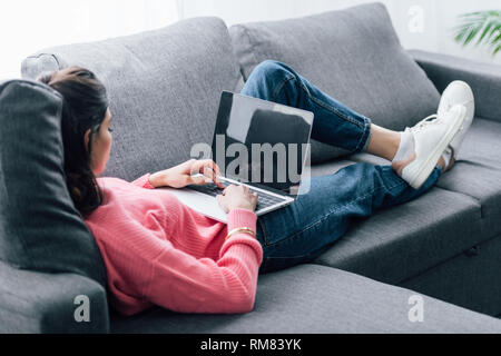 indian woman using laptop with blank screen while lying on sofa Stock Photo
