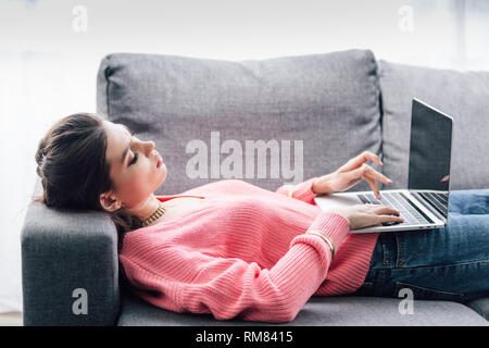 indian woman using laptop with blank screen while lying on sofa Stock Photo
