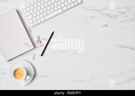 Office desk with computer, coffee cup, pink diary and paper clips on white marble background. Flat lay. Copy space for text. Top view. Stock Photo