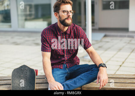 Bearded skater sitting on bench Stock Photo