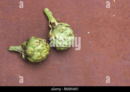 Two artichokes on a brown rusty metal texture with space to place other elements or texts Stock Photo