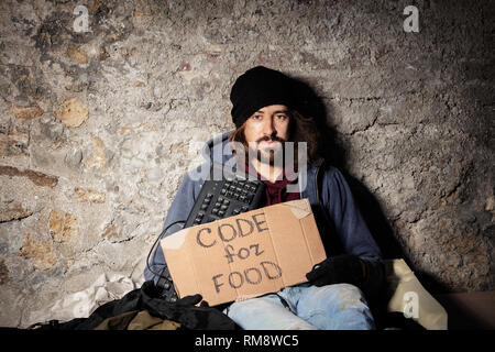 Man sits on floor with keyboard and cardboard sign Stock Photo