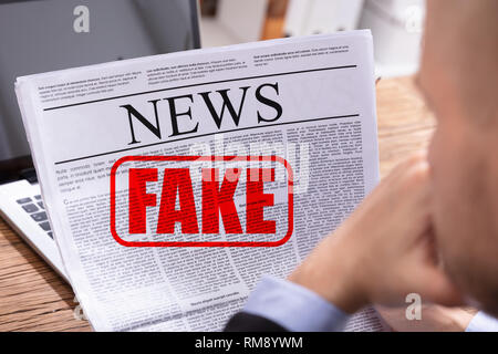 Man Reading Fake News In Newspaper Over Desk Stock Photo - Alamy