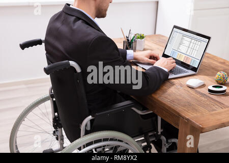 Disabled Businessman Sitting On Wheelchair Using Laptop At Workplace Stock Photo