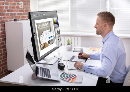 Male Designer's Hand Using Graphic Tablet While Working On Multiple Computers Stock Photo