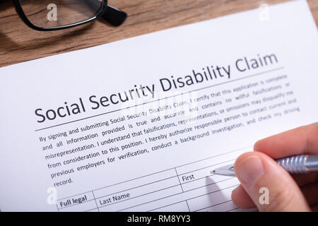 Close-up Of A Person's Hand Filling Social Security Disability Claim Form Stock Photo