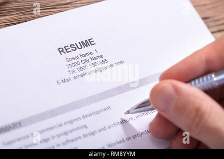 Close-up Of Businessman Holding Pen In Hand Reading Resume On Wooden Desk Stock Photo