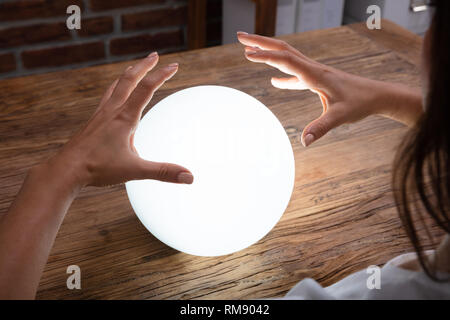 Close-up Of Fortuneteller's Hand Covering The Glowing Crystal Ball On Desk Stock Photo