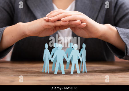 Close-up Of A Businesswoman's Hand Protecting Blue Paper Cut Out Human Figures Forming Circle Stock Photo
