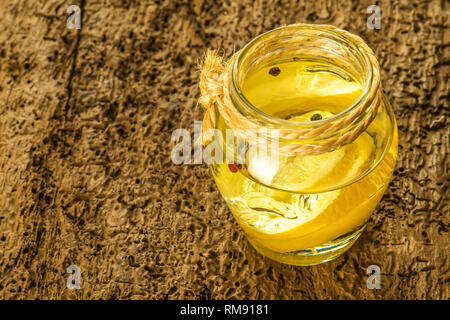 Olive oil flavored with lemon and peppercorns in glass bottle on old wooden table Stock Photo