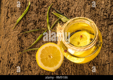 Olive oil flavored with lemon and red peppercorns in glass bottle on old wooden table Stock Photo