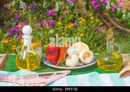 Extra virgin olive oil in vintage two glass jars, garlic, peppers, rosemary and mint on old table in summer garden Stock Photo