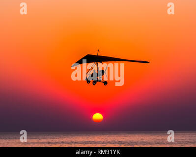 The person flying on a trike with the motor against The hang-glider is flying against the sunset. Stock Photo