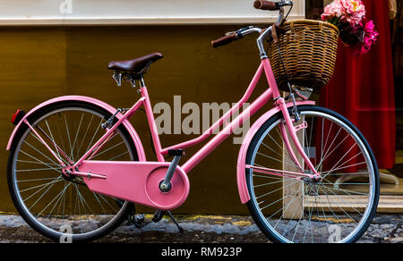 Pink ladies' bicycle with a basket stands against the wall. Stock Photo