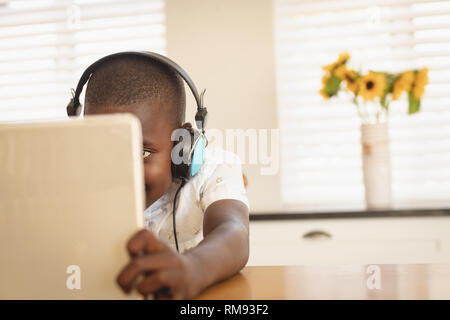 African American boy playing game on digital tablet at dining table in kitchen Stock Photo