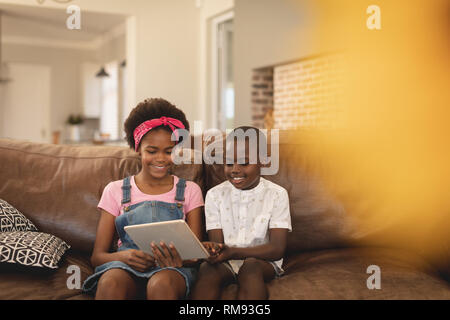 African American sibling sitting on the sofa and using digital tablet Stock Photo