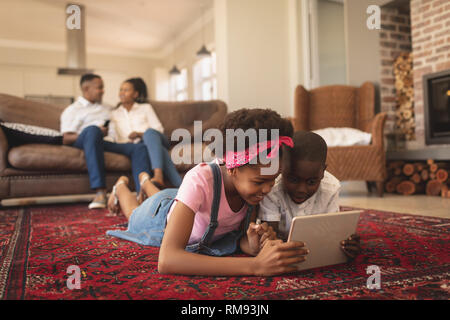 African American children lying on floor and using digital tablet while parents sitting on the sofa Stock Photo