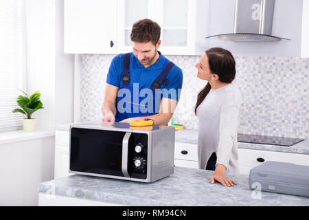 Pretty Woman Standing Near Repairman Repairing Oven Using Digital Multimeter In Kitchen Stock Photo
