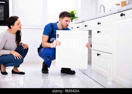 Woman Looking At Male Handyman Installing Cabinet Door In The Kitchen Stock Photo