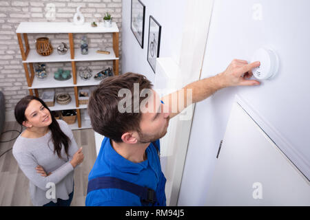 Pretty Woman Standing Near Repairman Installing Smoke Detector On Wall At Home Stock Photo
